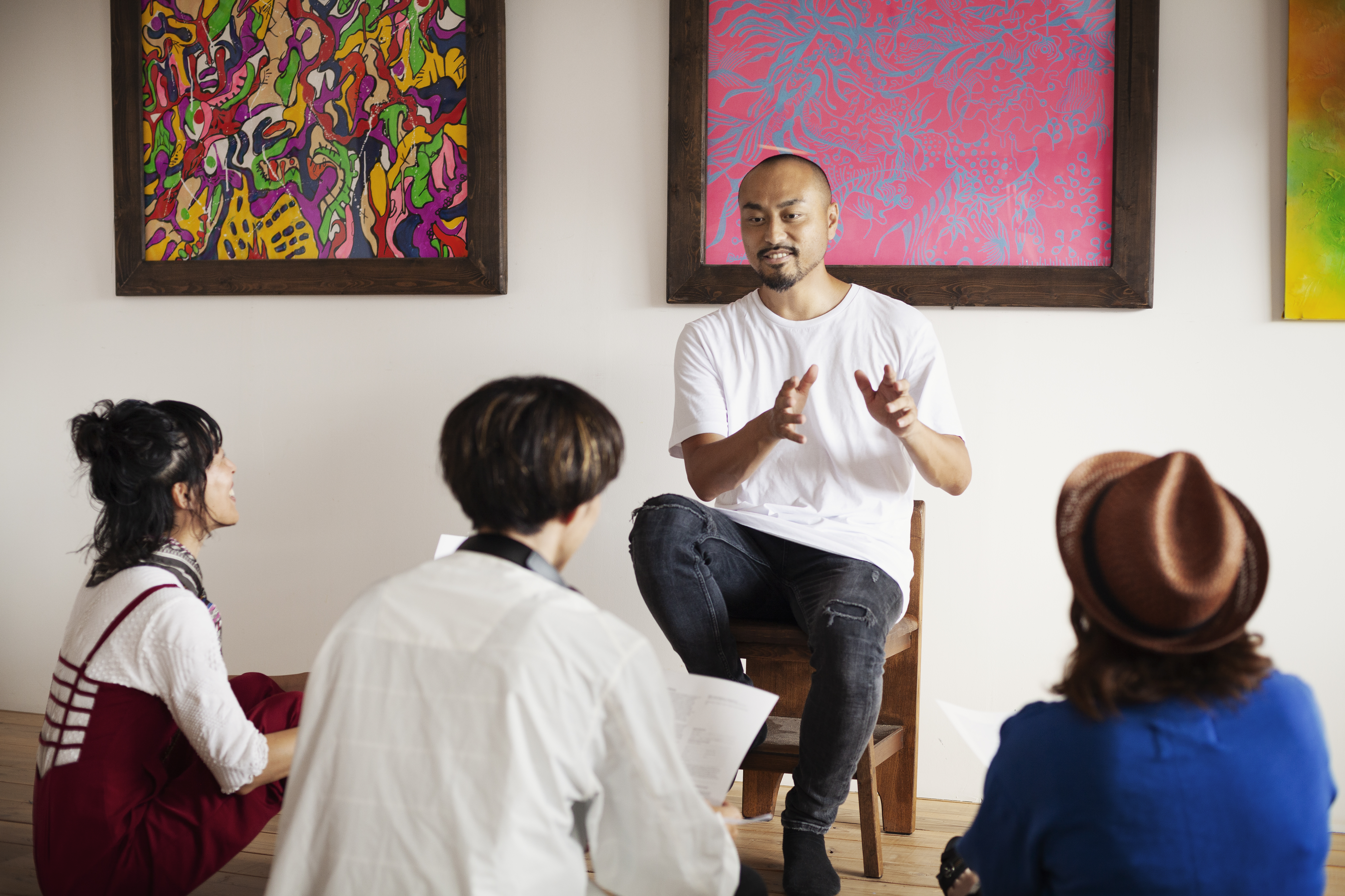 Group of men and women sitting in art gallery, holding a discussion.