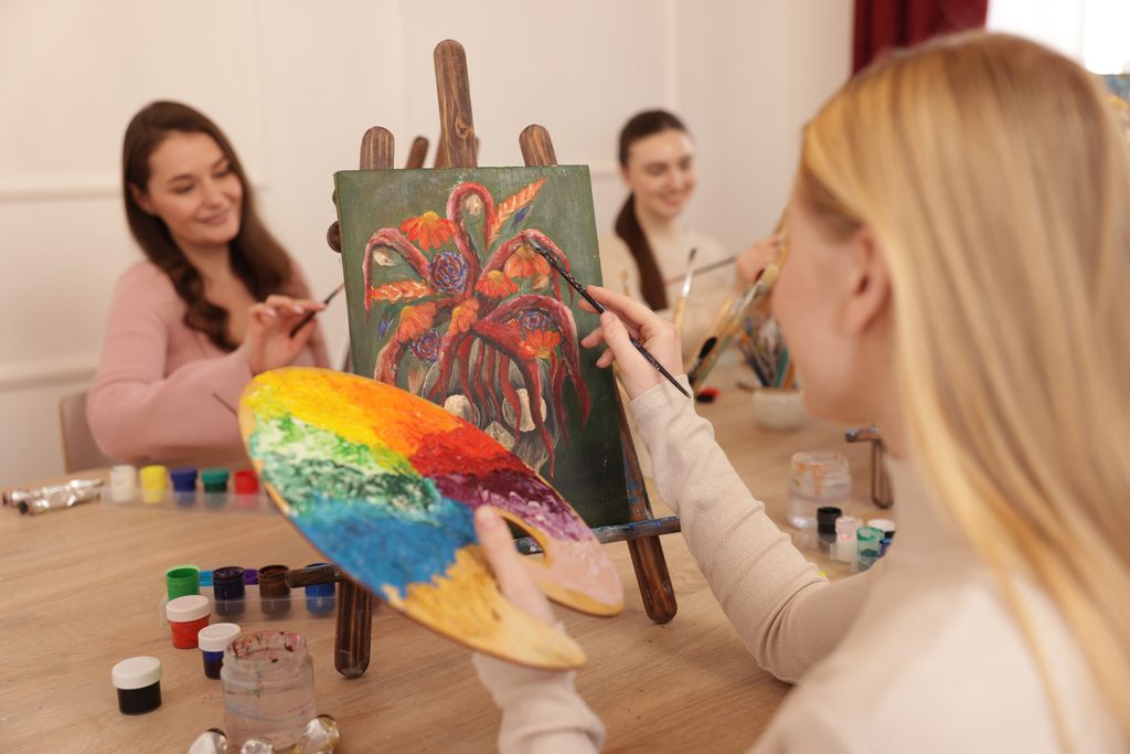 Group of young women enjoy an art class, painting flowers together